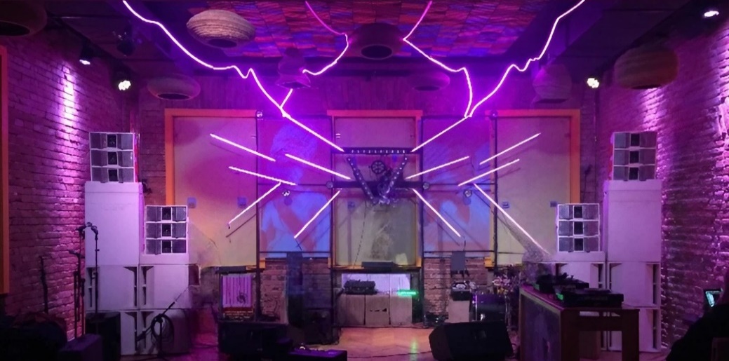 White speaker cabinets installed around a performance space with purple stage lighting.