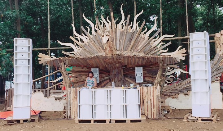 White Kannonaudio speaker towers flank a DJ booth on a wooden stage in the forest.
